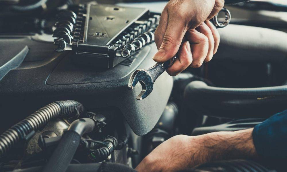 A person with a wrench in his/her hand repairing the engine of a car.